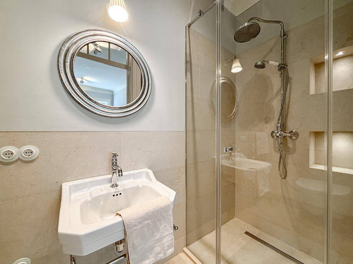 Elegantes Badezimmer mit Einzelwaschbecken, rundem Spiegel und geräumiger Duschkabine.