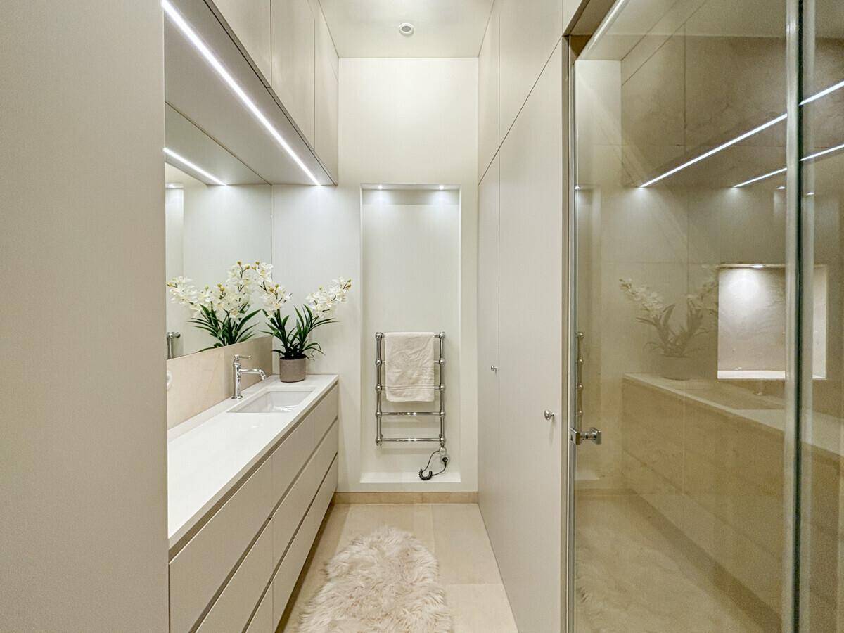 Modernes, schmales Badezimmer mit Doppelwaschbecken, integrierter Beleuchtung und begehbarer Dusche.