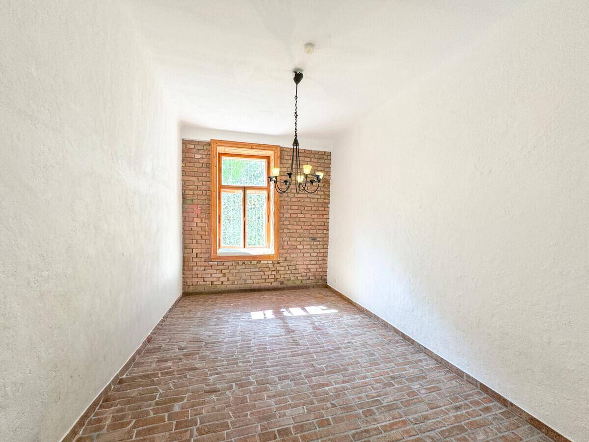 Geräumiger Innenraum mit unverputzter Ziegelwand, Terrakottaboden und einem schmiedeeisernen Kronleuchter.