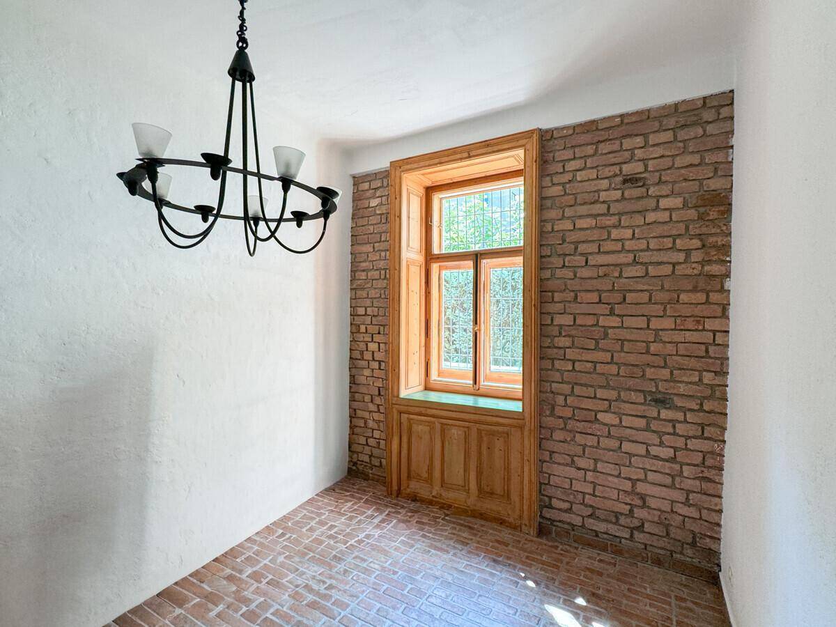 Heller Raum mit freigelegter Ziegelwand, Terrakottaboden und einem Fenster mit Holzrahmen.