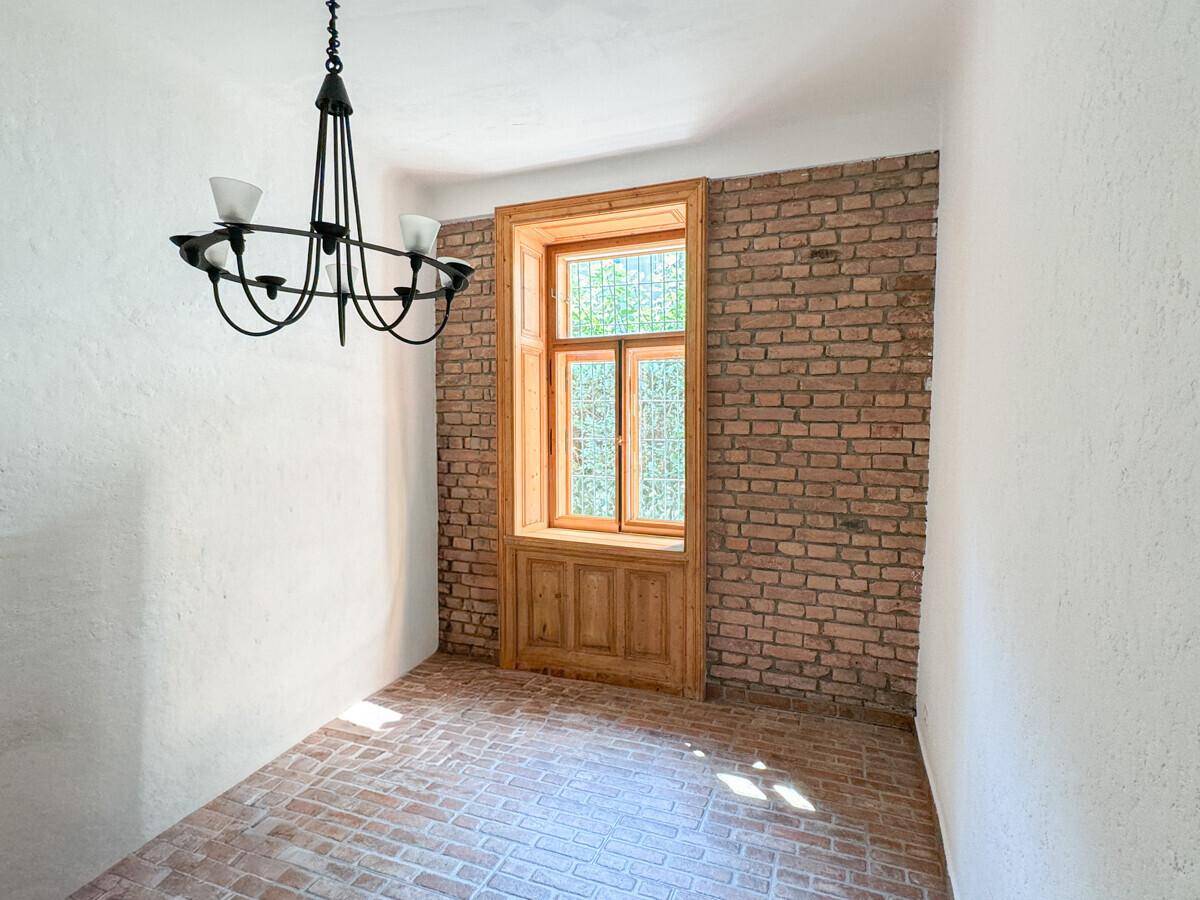 Charmanter Raum mit Ziegelwand, Terrakottaboden und einem hohen Fenster mit Holzverkleidung.