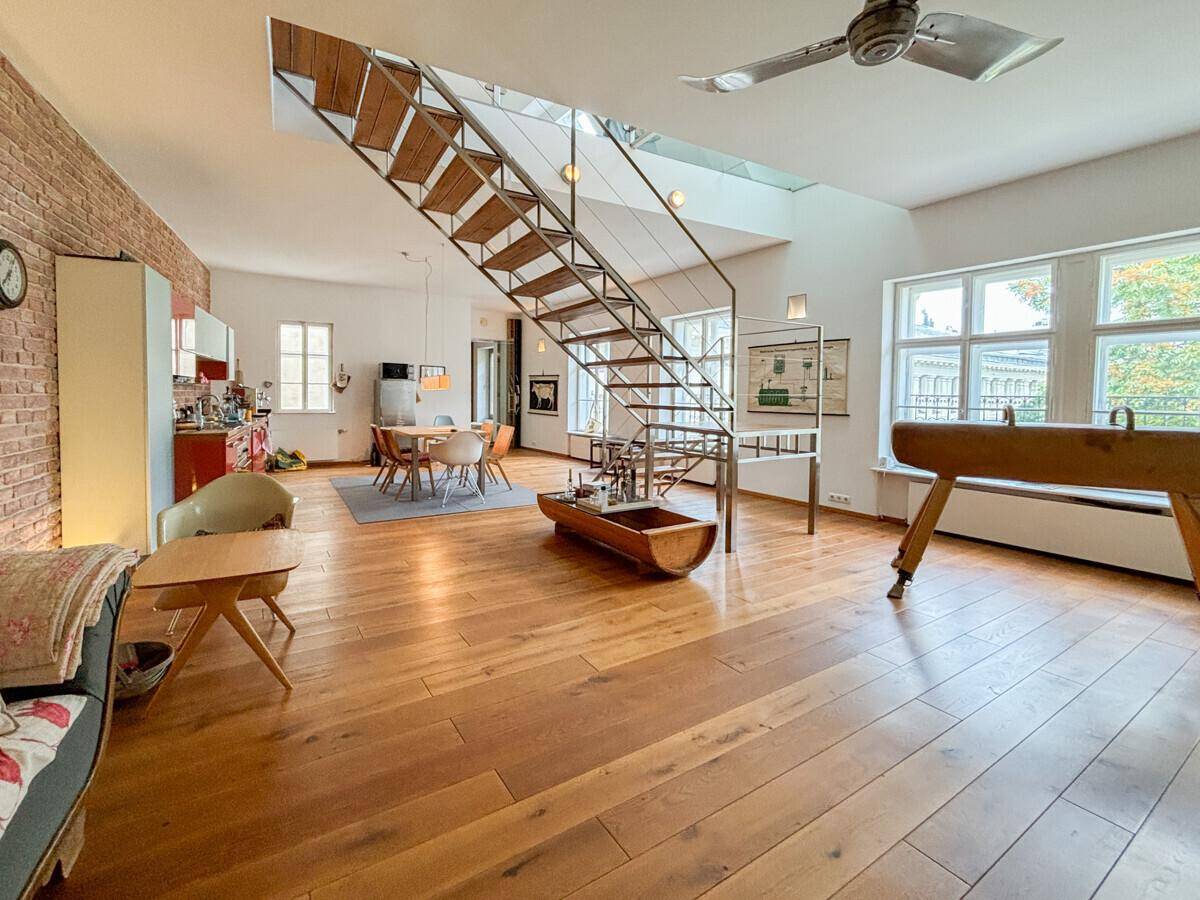 Geräumiger offener Wohnbereich mit Holzboden, moderner Treppe, Essbereich und kleiner Küche.