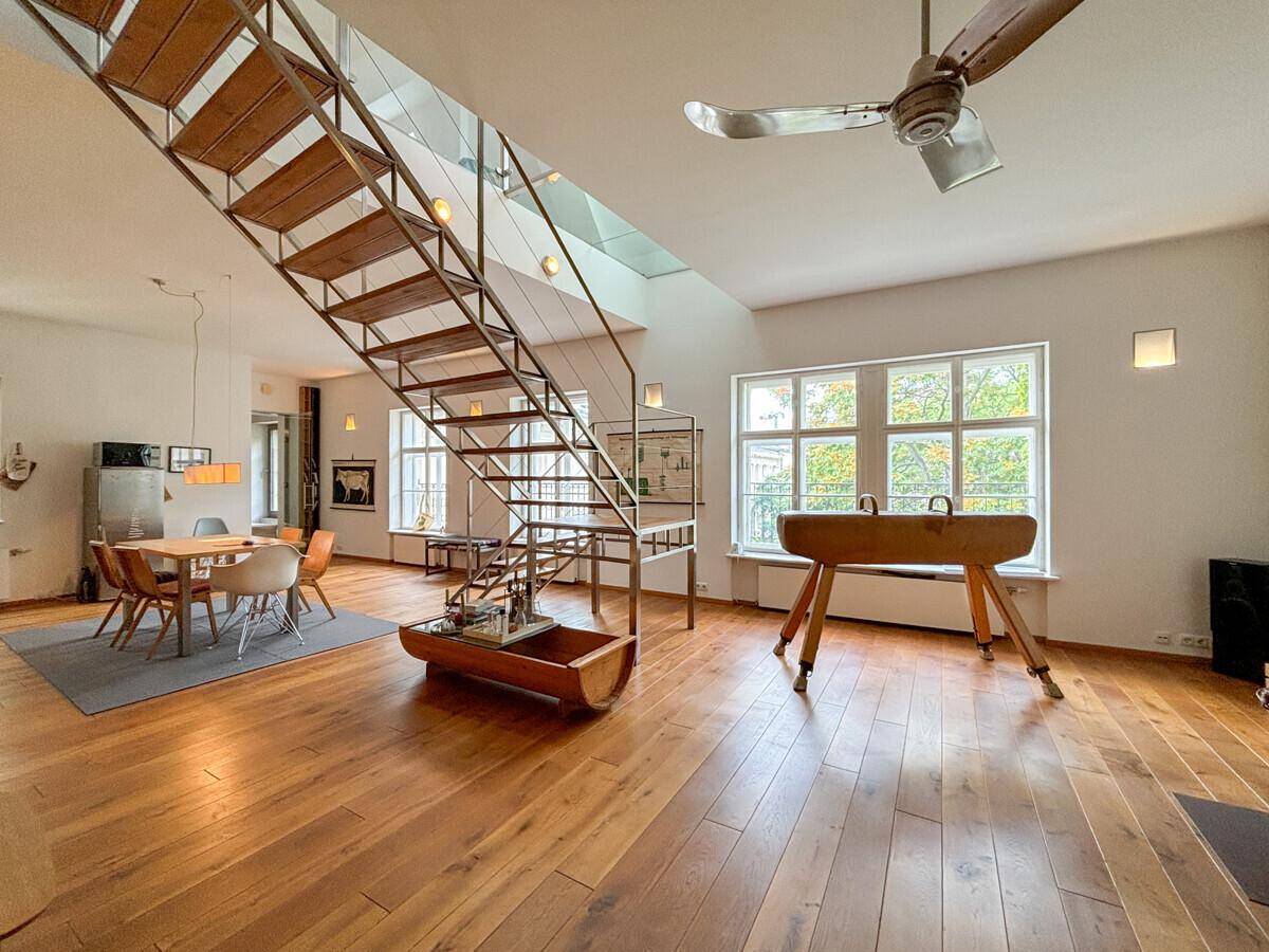 Offener Wohnbereich mit markanter Treppe, Holzboden, viel Tageslicht und einem modernen Kaminofen.