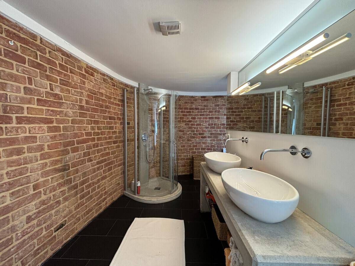 Modernes Badezimmer mit freigelegten Ziegelwänden, Doppelwaschbecken und einer geräumigen Dusche.