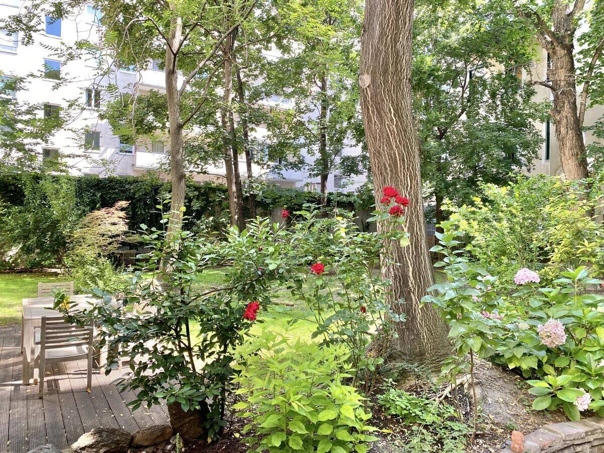 Gepflegter Gartenbereich mit Bäumen, Sträuchern und einer Holzterrasse für entspannte Stunden.