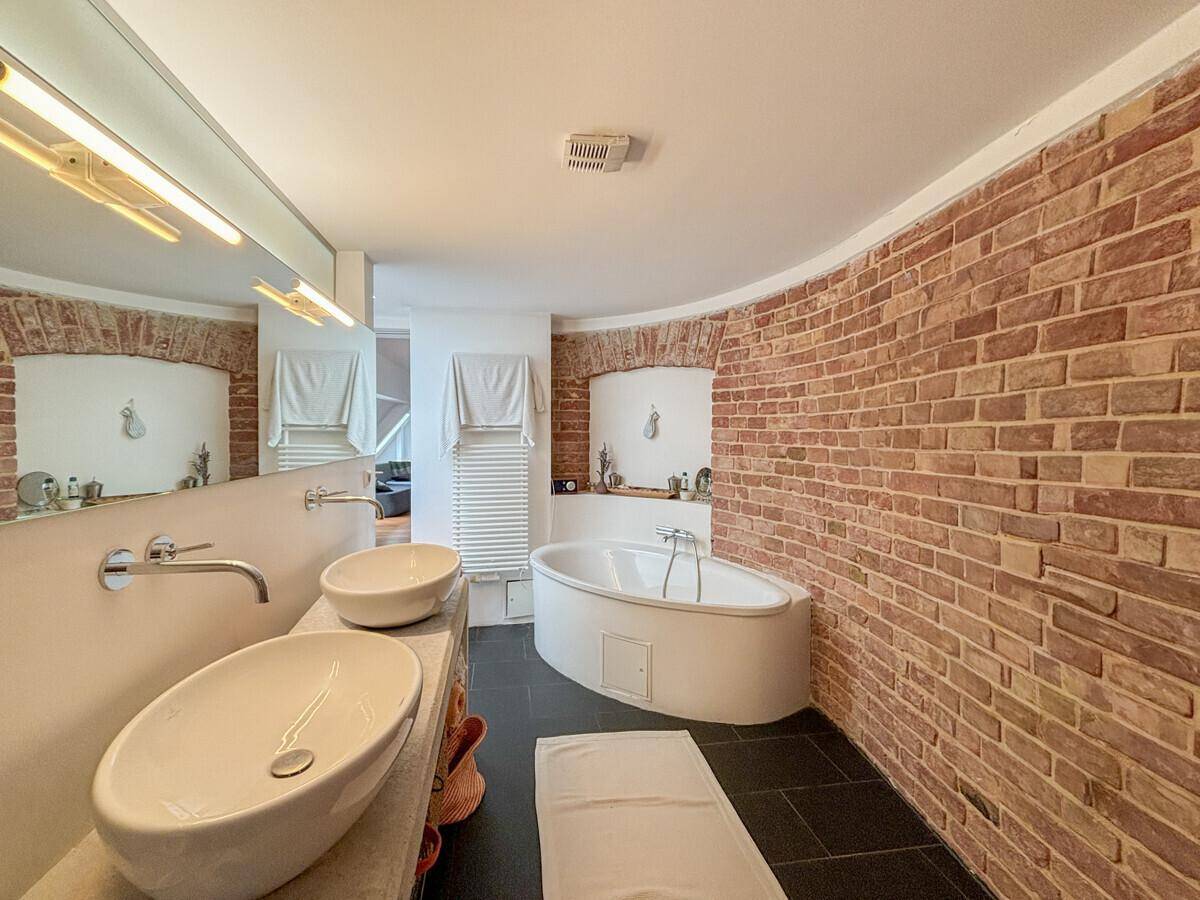 Geräumiges Badezimmer mit Ziegelwänden, Doppelwaschbecken und einer modernen Badewanne.