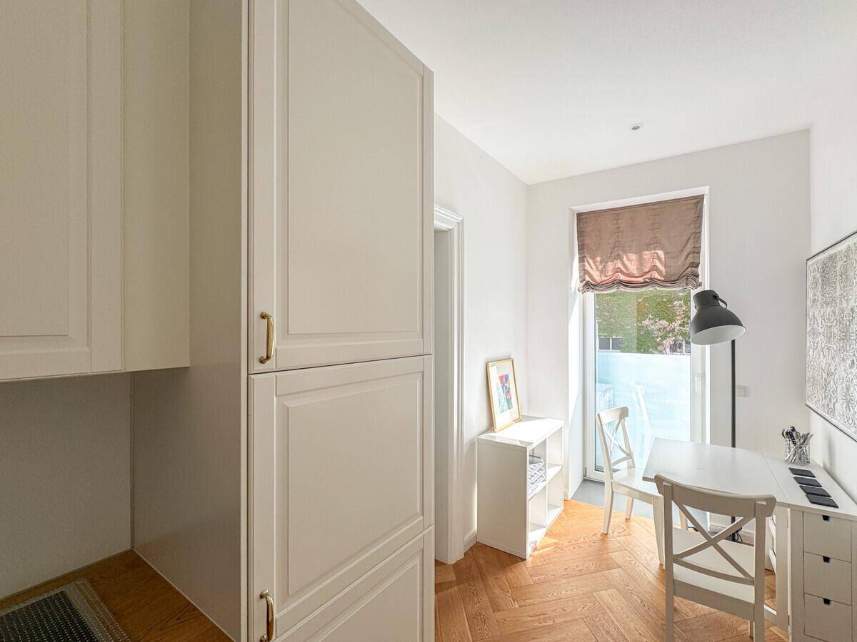 Heller Arbeitsbereich mit Schreibtisch am Fenster, weißem Mobiliar und natürlichem Lichteinfall.