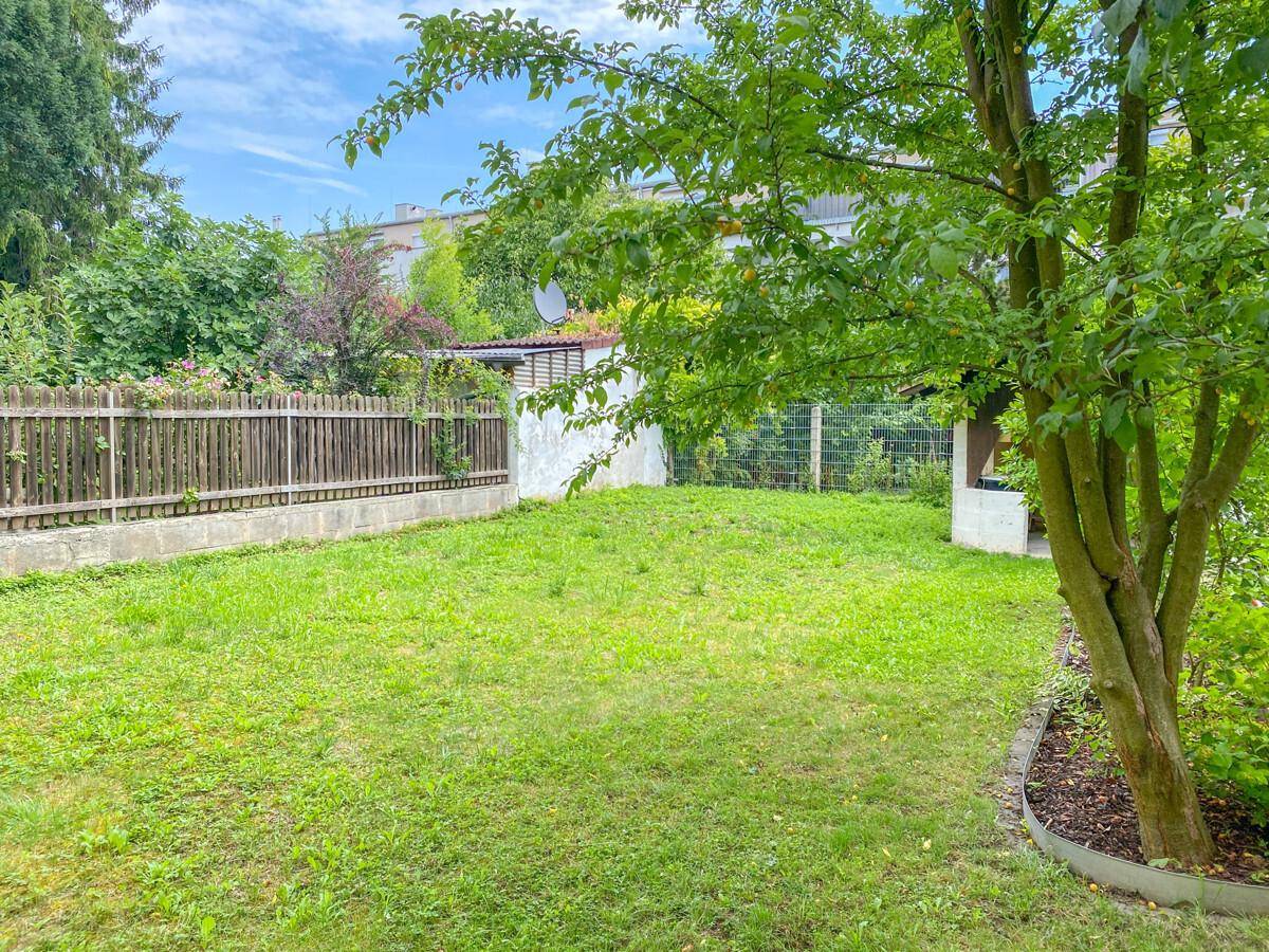 Gepflegter Gartenbereich mit grünem Rasen, Holzzaun und schattenspendenden Bäumen.