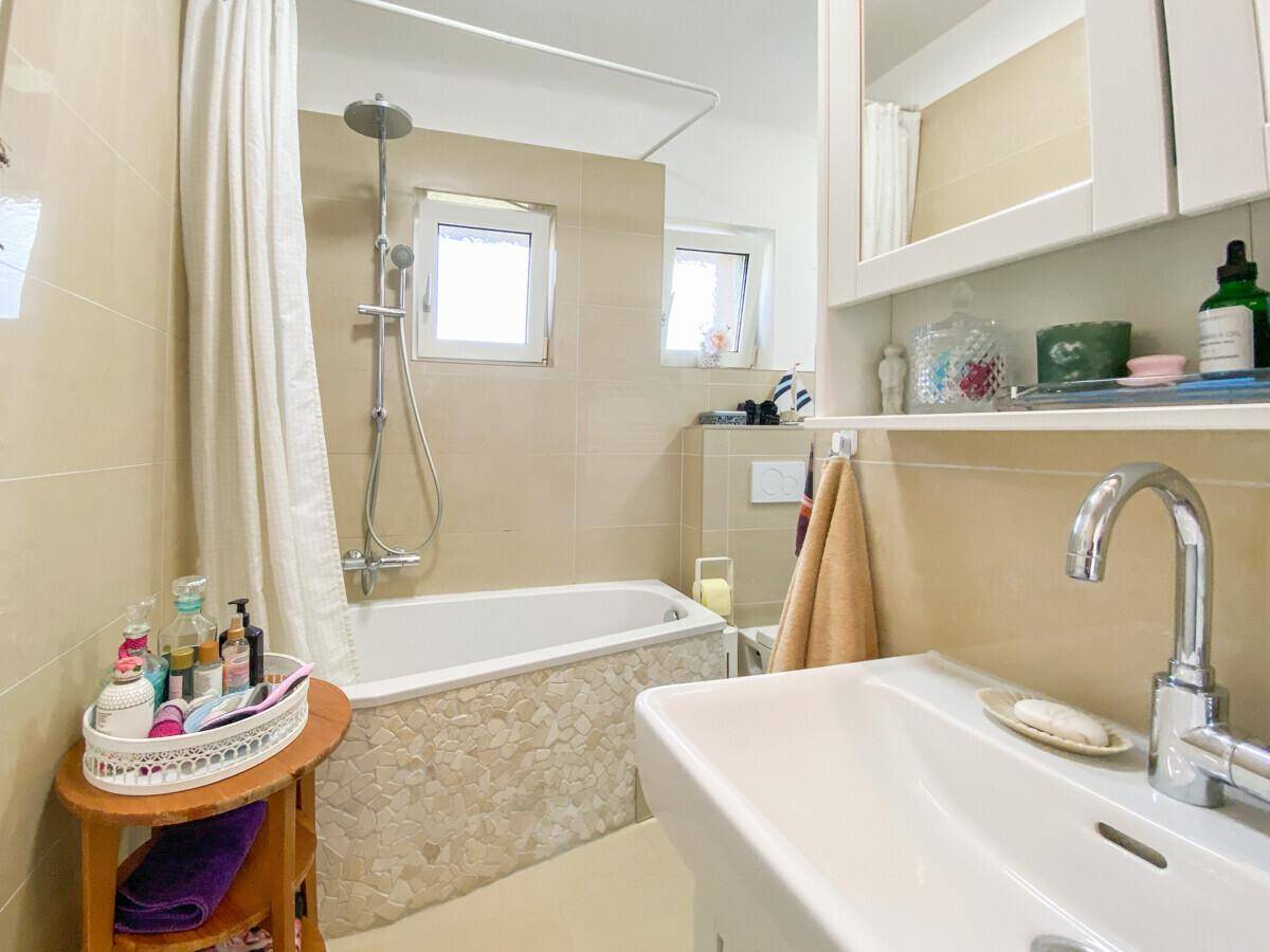 Helles Badezimmer mit Badewanne, Duschvorhang, Einzelwaschbecken und Fenster für Tageslicht.