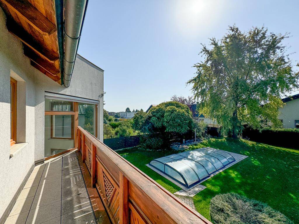 Balkon mit Holzboden und Geländer, bietet einen weiten Blick über den Garten und die Umgebung.