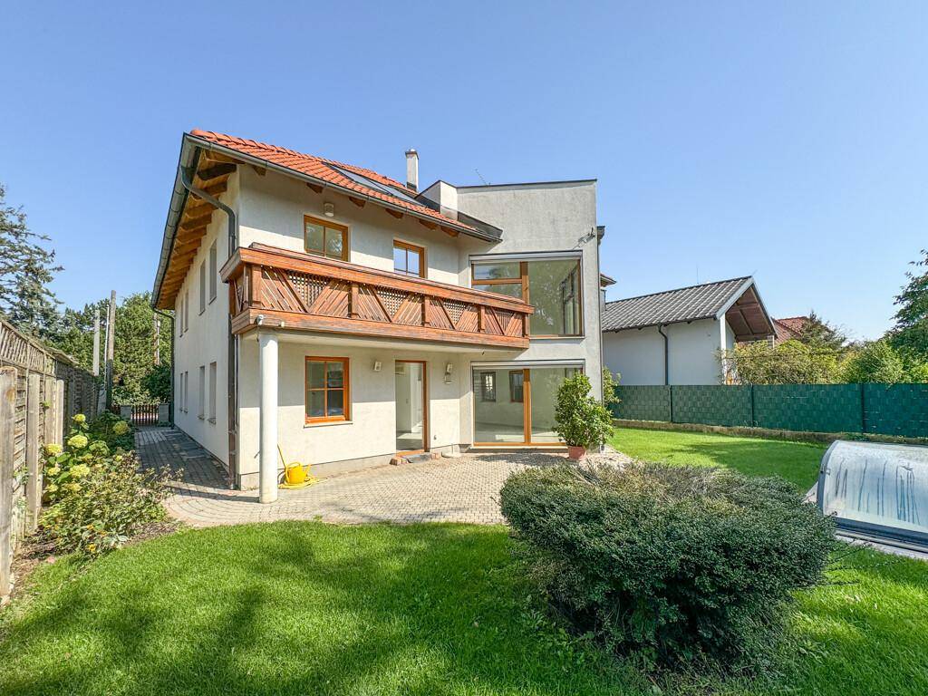 Rückansicht des Hauses mit Terrasse, Garten und überdachtem Swimmingpool unter blauem Himmel.