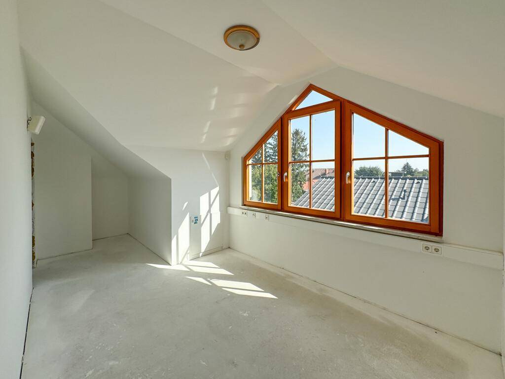 Helles Dachgeschosszimmer mit schrägen Wänden, großen Fenstern und Blick ins Grüne.
