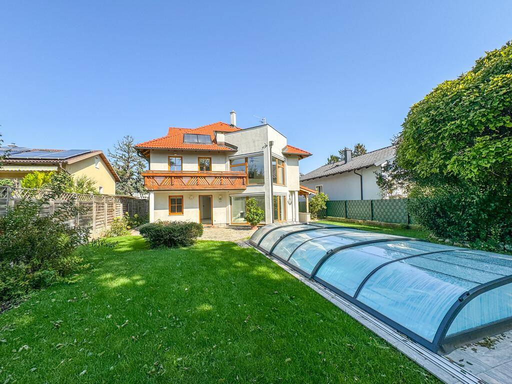 Weitläufiger Garten mit Rasenfläche, überdachtem Pool und Blick auf die Hausfassade.