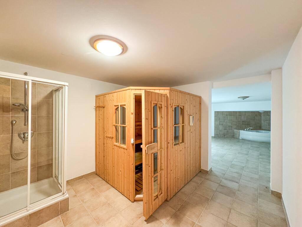 Wellnessbereich mit Sauna, Duschkabine und Zugang zu einem weiteren Raum mit Whirlpool.