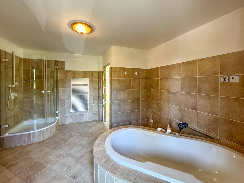 Geräumiges Badezimmer mit Badewanne, Duschkabine, Fliesenboden und beheiztem Handtuchhalter.