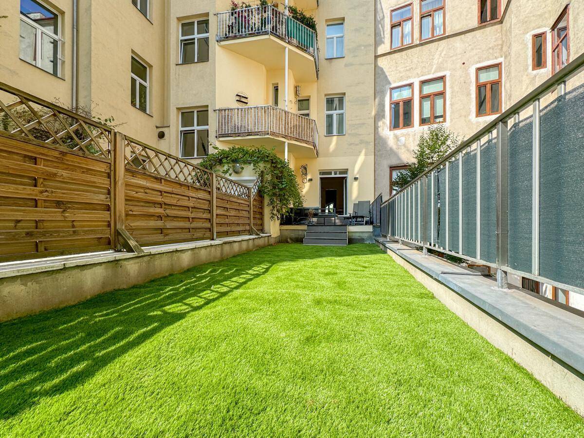 Gepflegter Gartenbereich mit Kunstrasen und Blick auf die Gebäudefassade.