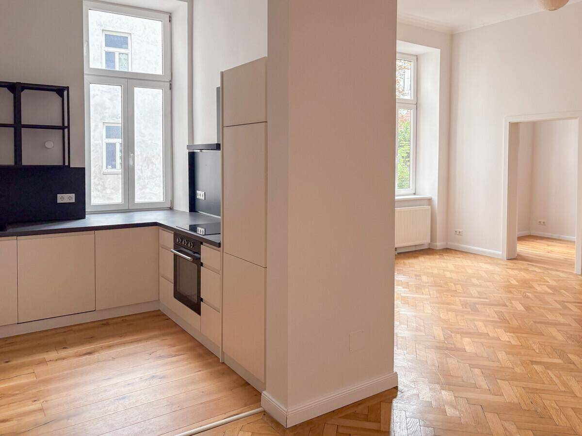 Offener Küchenbereich mit moderner Einbauküche und Fischgrätparkett, angrenzend an einen Wohnraum.