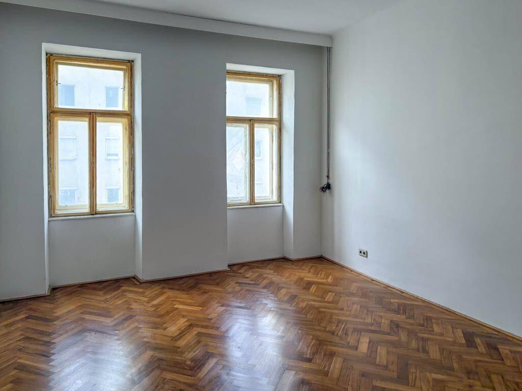 Heller, leerer Raum mit klassischem Fischgrätparkett und zwei Fenstern, ideal für individuelle Gestaltung.