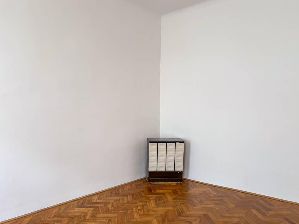 Ecke eines leeren Raumes mit Fischgrätparkett und einem traditionellen Ofen in der Ecke.