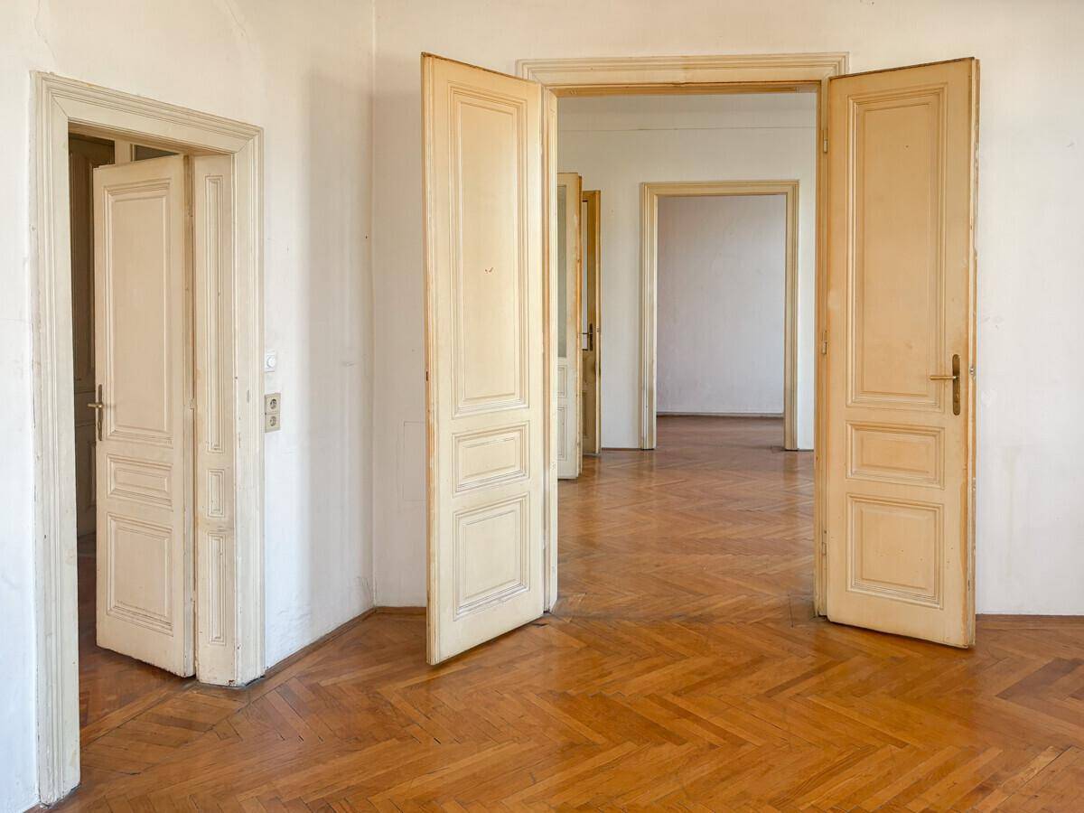 Großzügiger Raum mit Fischgrätparkett und einer Reihe von Flügeltüren, die weitere Zimmer verbinden.