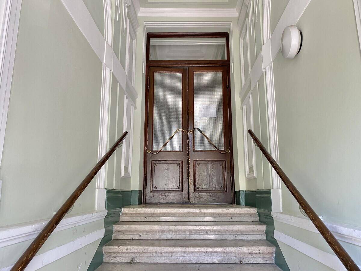 Historischer Eingangsbereich mit Holztüren, verzierten Handläufen und Marmorstufen.