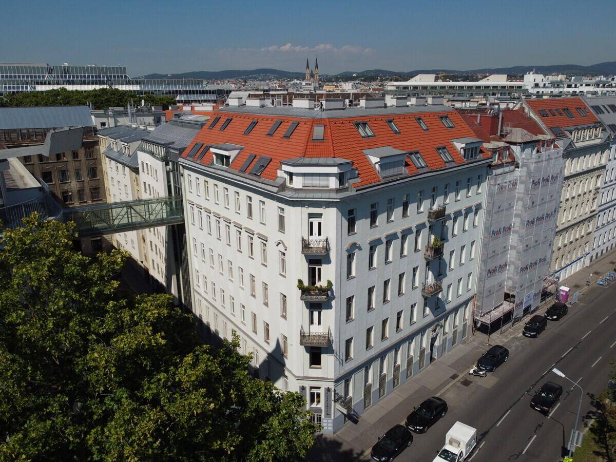 Luftaufnahme eines historischen Gebäudes mit rotem Mansarddach und Balkonen in urbaner Umgebung.