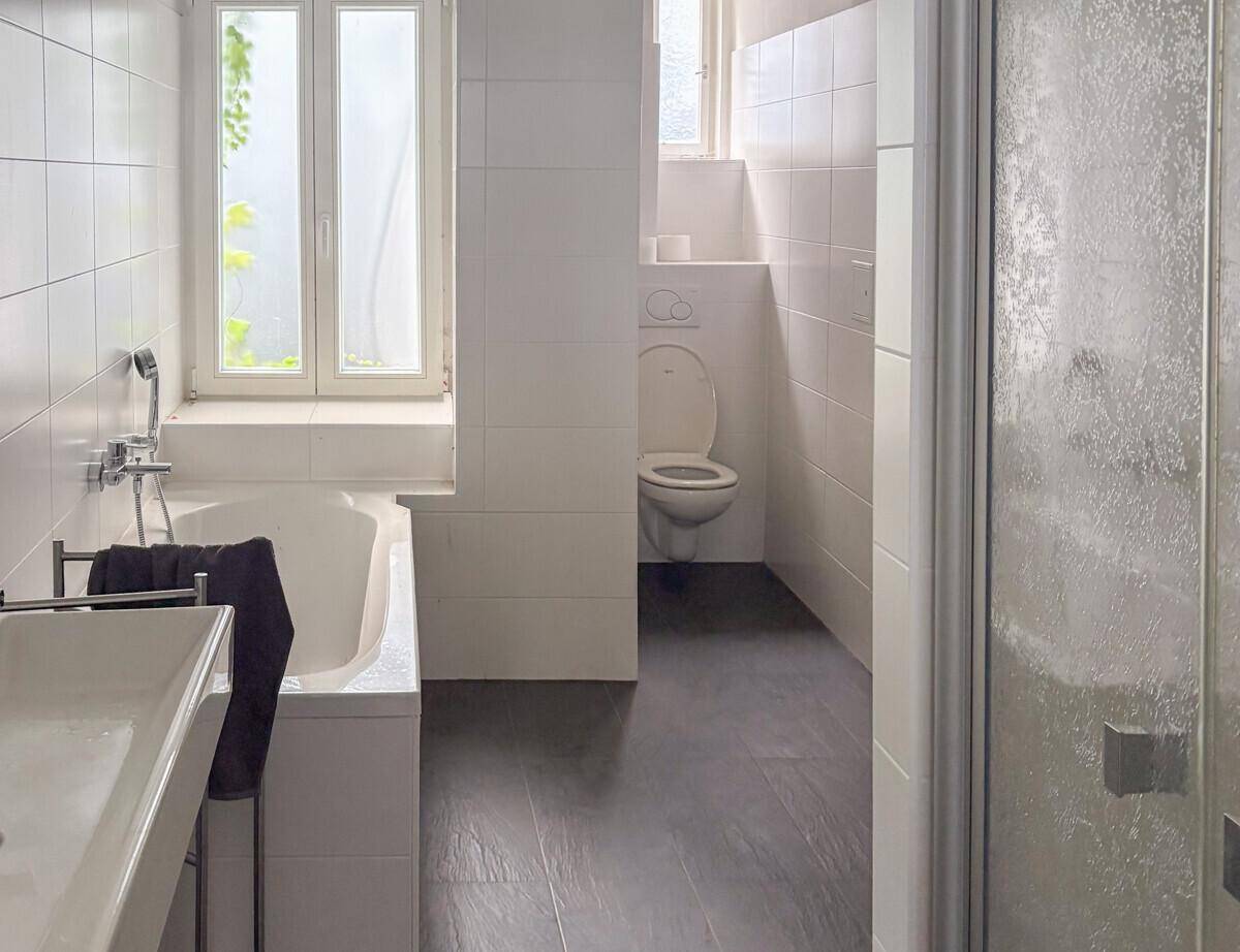 Helles Badezimmer mit Badewanne, Dusche, WC und weißen Fliesen.