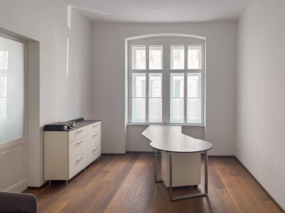 Geräumiges Büro mit Holzboden, weiß gestrichenen Wänden und einem modernen Schreibtisch.