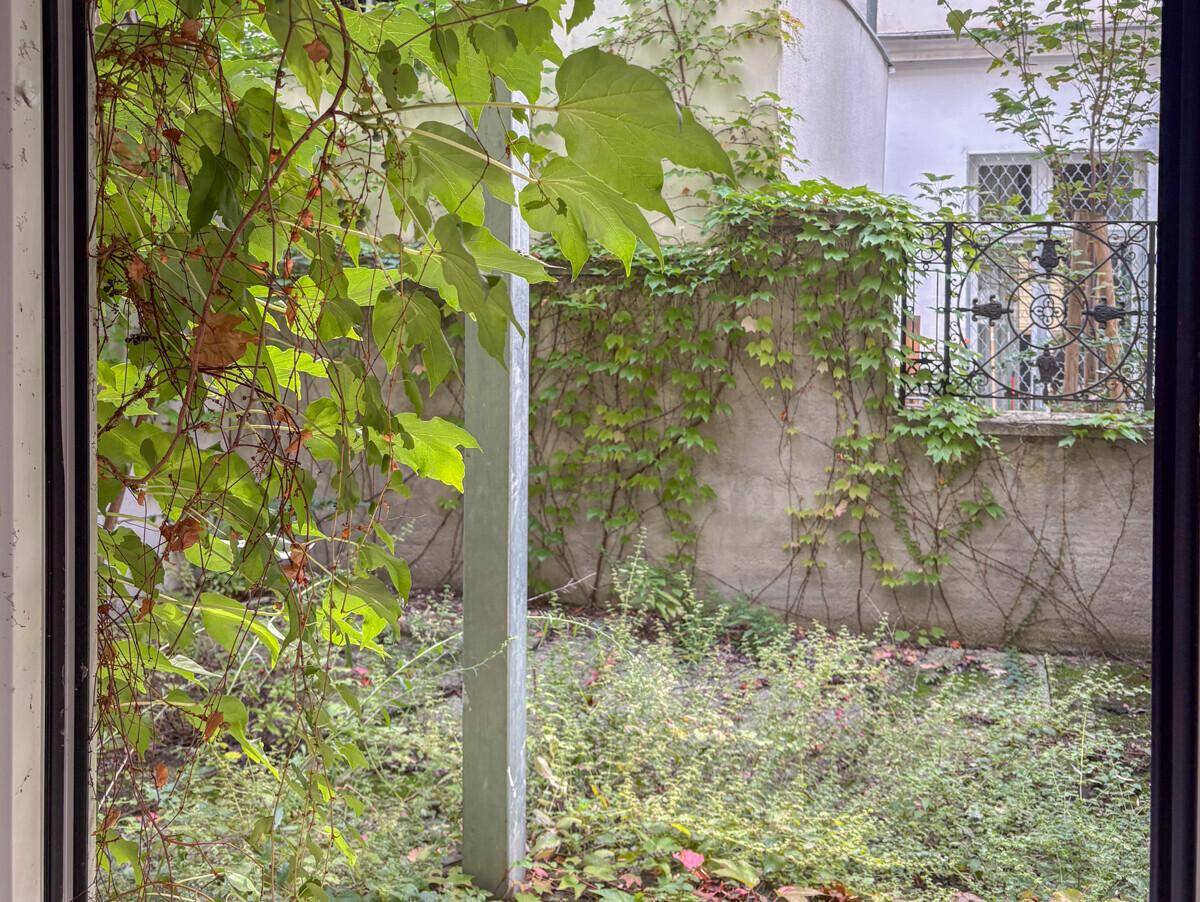 Ruhiger Innenhofgarten mit viel Grün, Kletterpflanzen und einem schmiedeeisernen Gitter.
