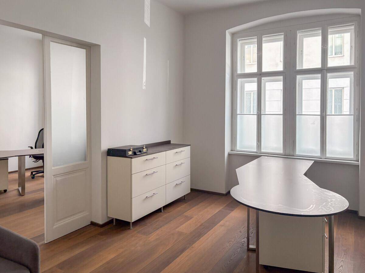 Helles Büro mit Holzboden, großem Fenster und modernem Schreibtisch.