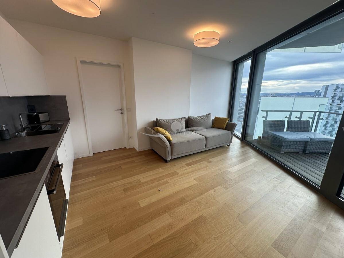 Heller Wohnbereich mit Sofa, integrierter Küchenzeile und großen Fenstern mit Stadtblick.