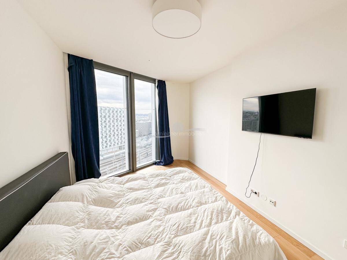 Modernes Schlafzimmer mit großem Bett, Holzboden und wandmontiertem Fernseher.