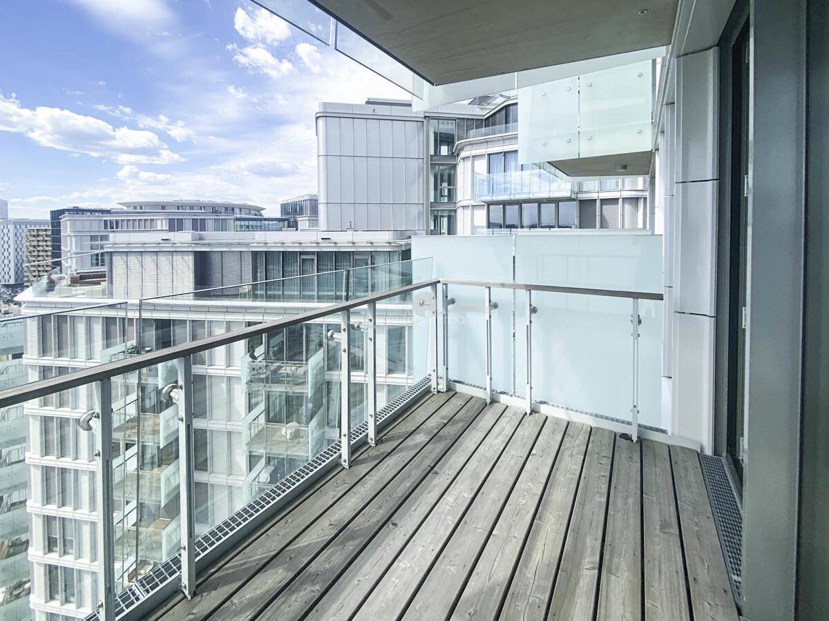 Geräumiger Balkon mit Holzfußboden und Glasgeländer, umgeben von moderner Architektur.