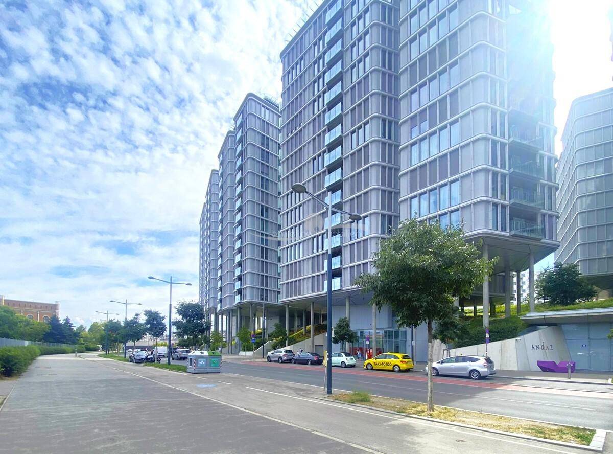 Moderne Hochhäuser entlang einer Straße mit Bäumen und parkenden Autos unter blauem Himmel.