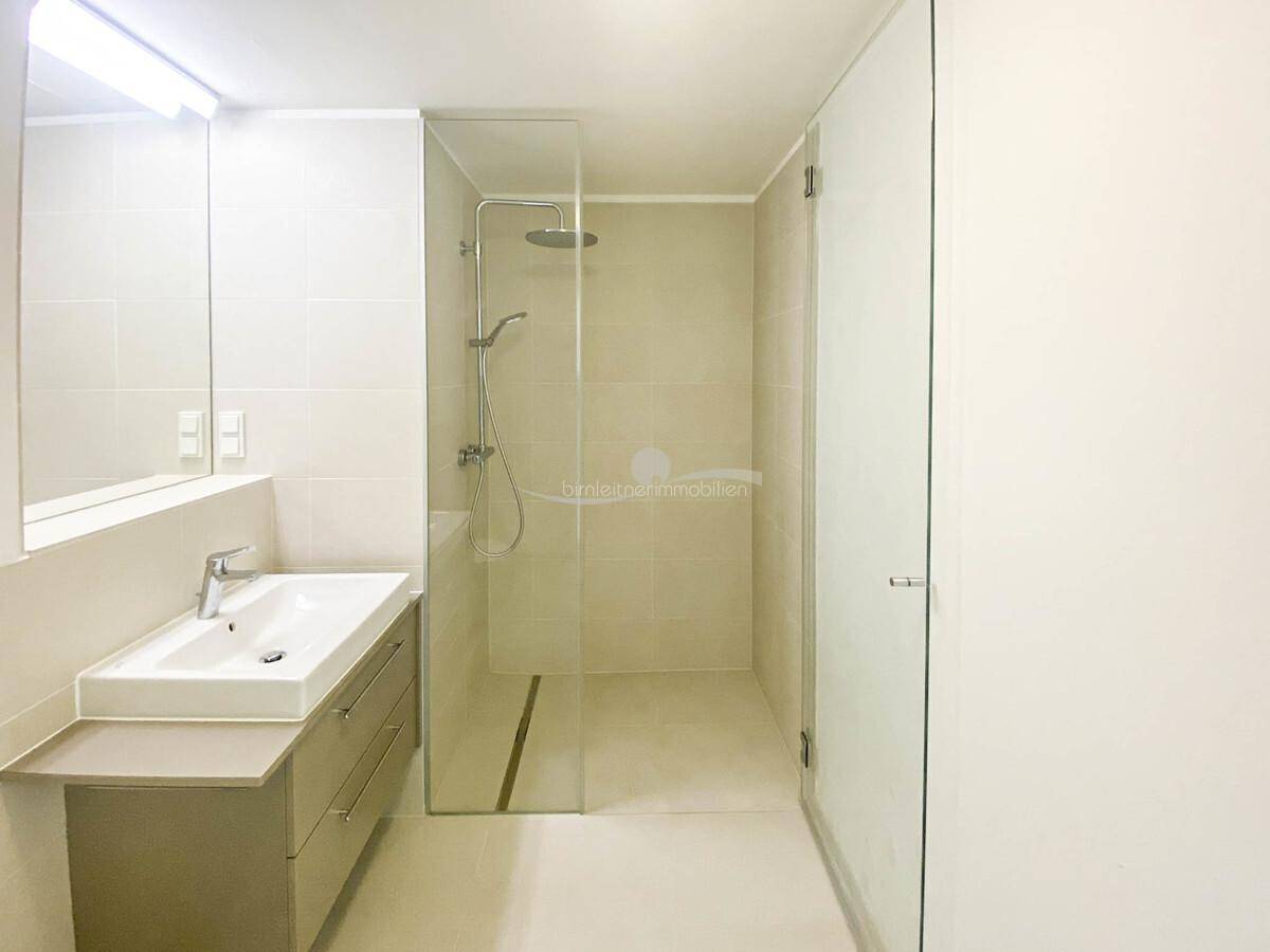 Modernes Badezimmer mit begehbarer Dusche, einzelnen Waschbecken und hellen Fliesen.