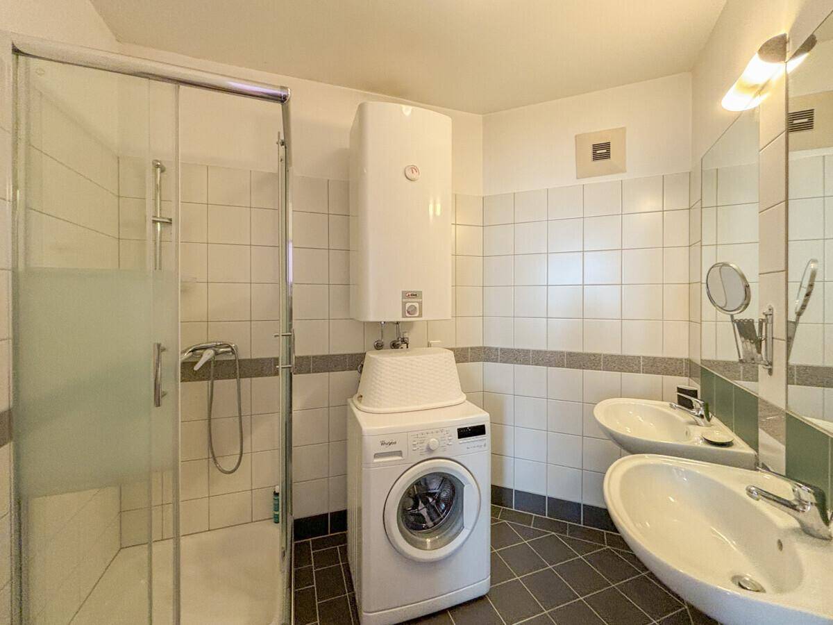 Badezimmer mit Dusche, zwei Waschbecken und integrierter Waschmaschine.