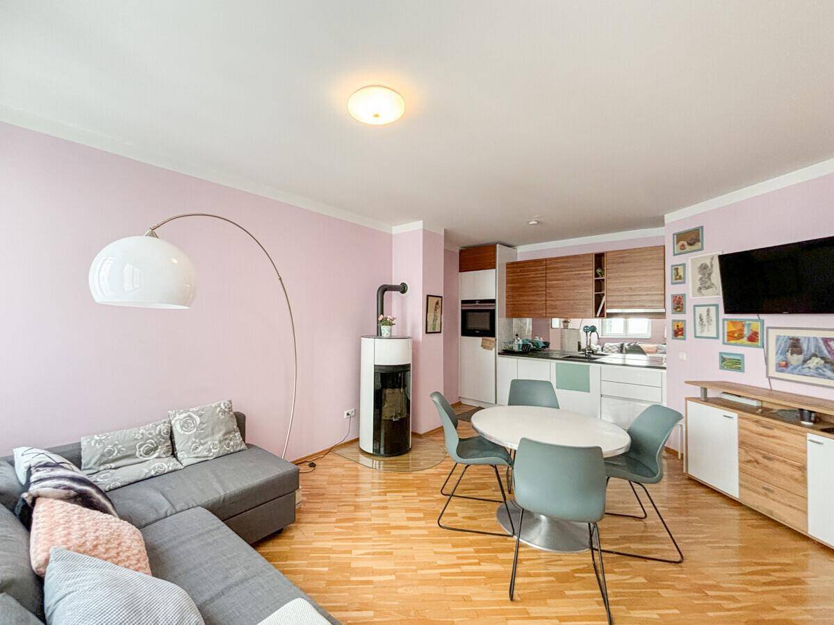 Gemütlicher Wohnbereich mit Sofa, Kaminofen und integrierter Küchenzeile in Pastellfarben.