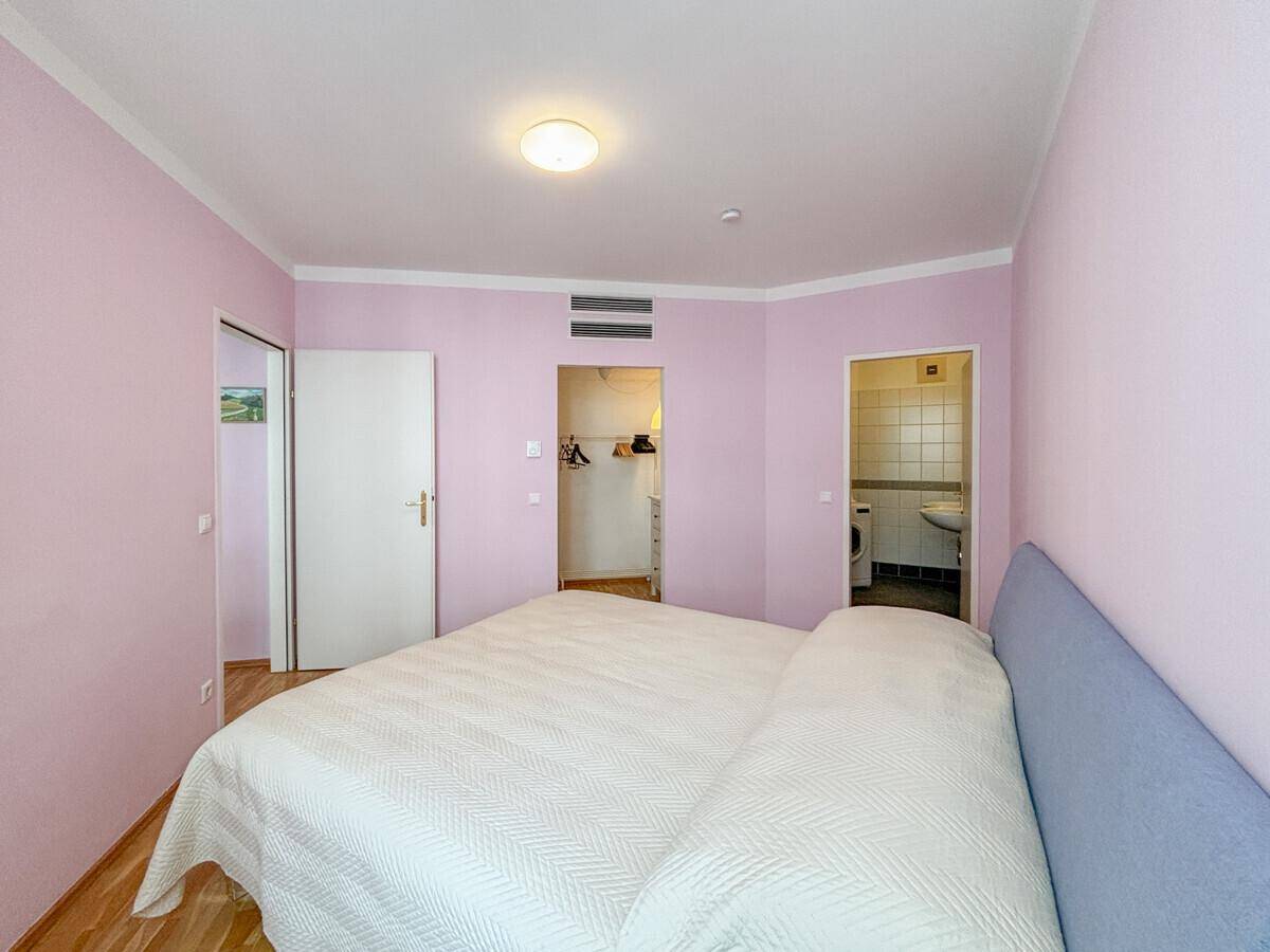 Schlafzimmer mit Doppelbett, Parkettboden und Zugang zu einem begehbaren Kleiderschrank.