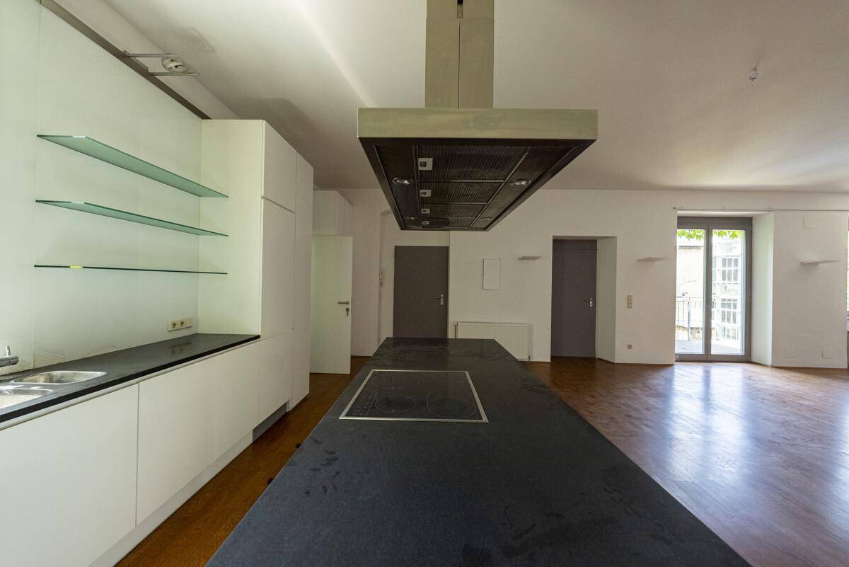 Moderne Küche mit weißen Schränken, schwarzer Arbeitsplatte und Kochinsel mit Induktionskochfeld.