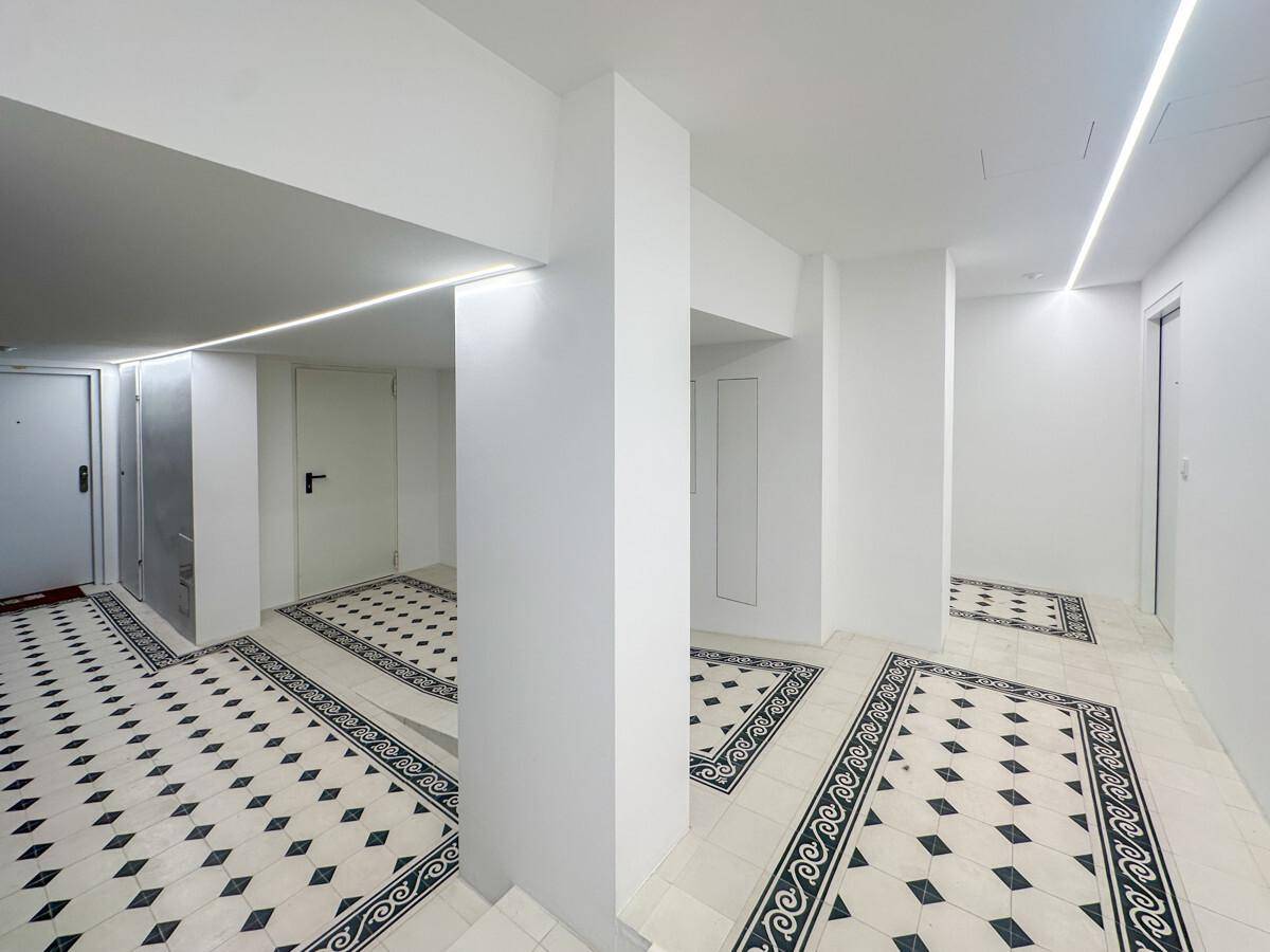 Heller Flur mit auffälligem Fliesenbodenmuster und modernen, integrierten Lichtleisten an den Wänden.