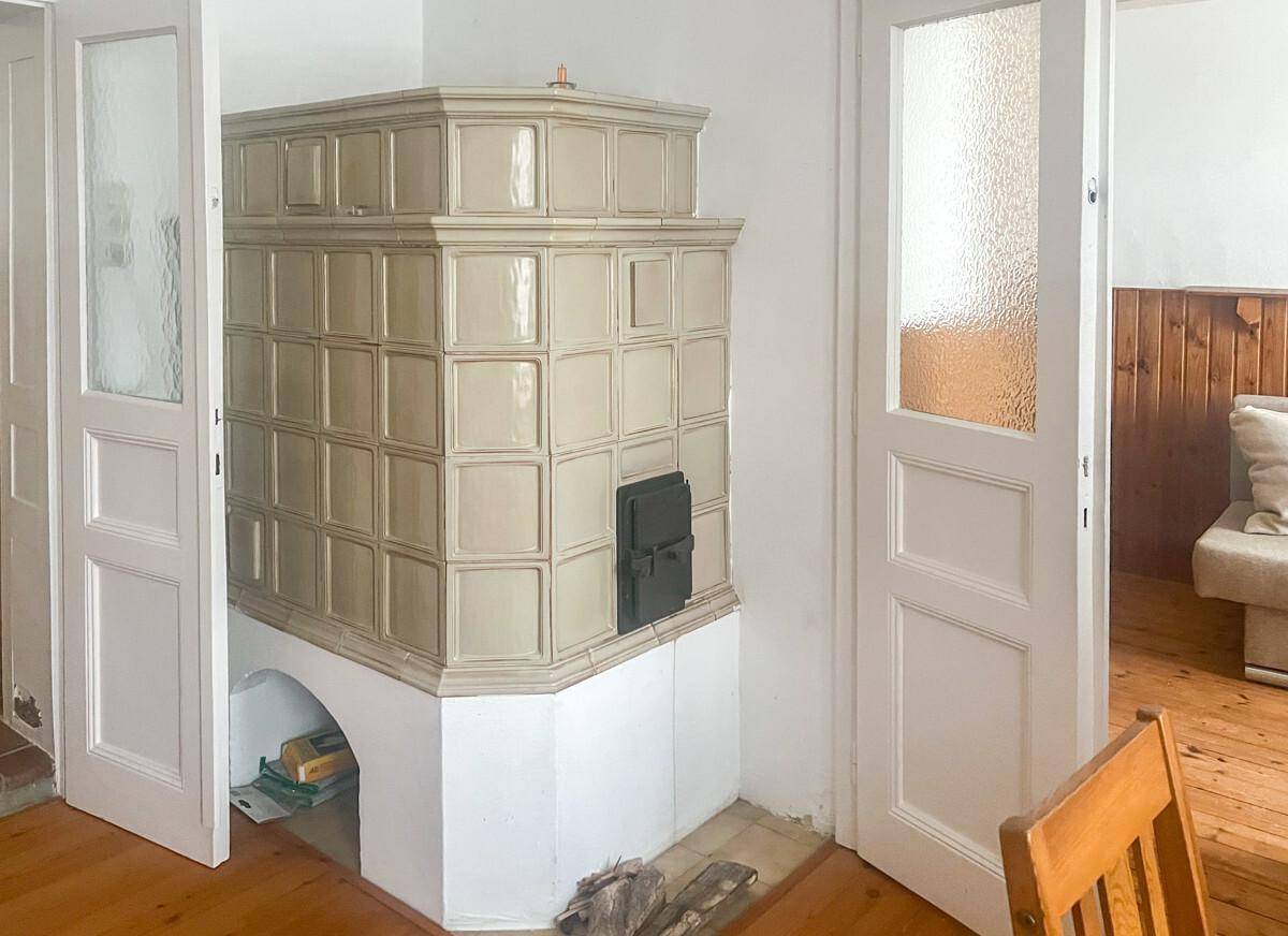 Großer, traditioneller Kachelofen als zentrales Element zwischen zwei Zimmertüren.