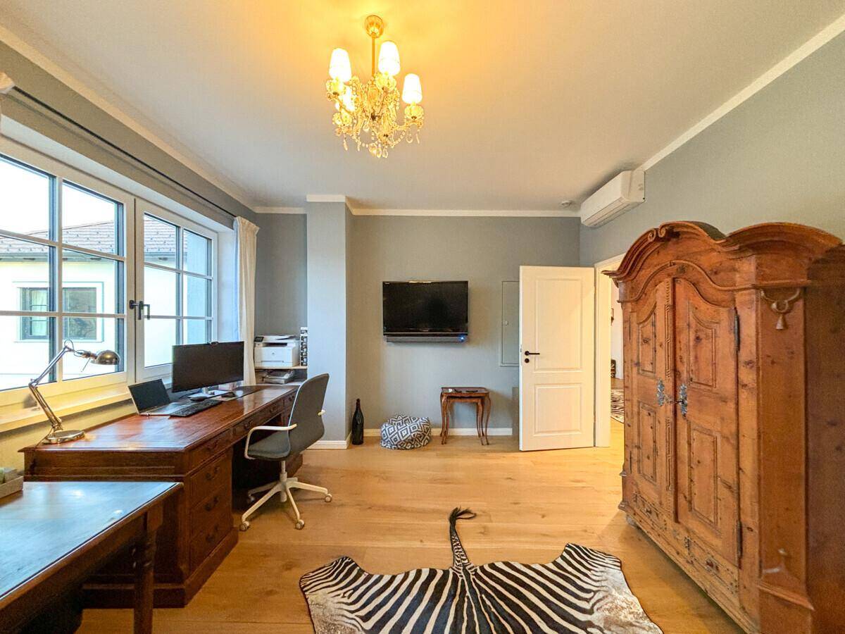 Geräumiges Arbeitszimmer mit großem Holzschreibtisch, antikem Schrank und Klimaanlage.