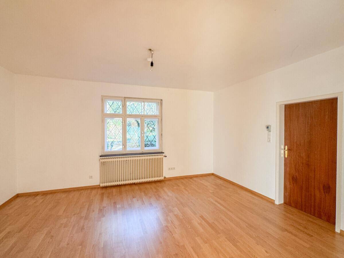 Helles Zimmer mit Holzboden, Fenster und einer schlichten Holztür.