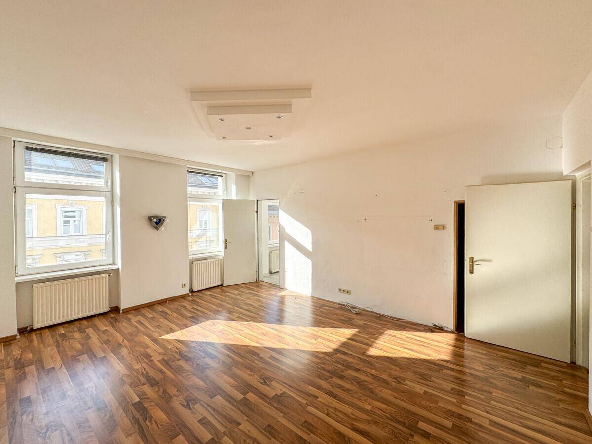 Helles, leeres Zimmer mit Laminatboden und viel natürlichem Licht, bereit zur Gestaltung.