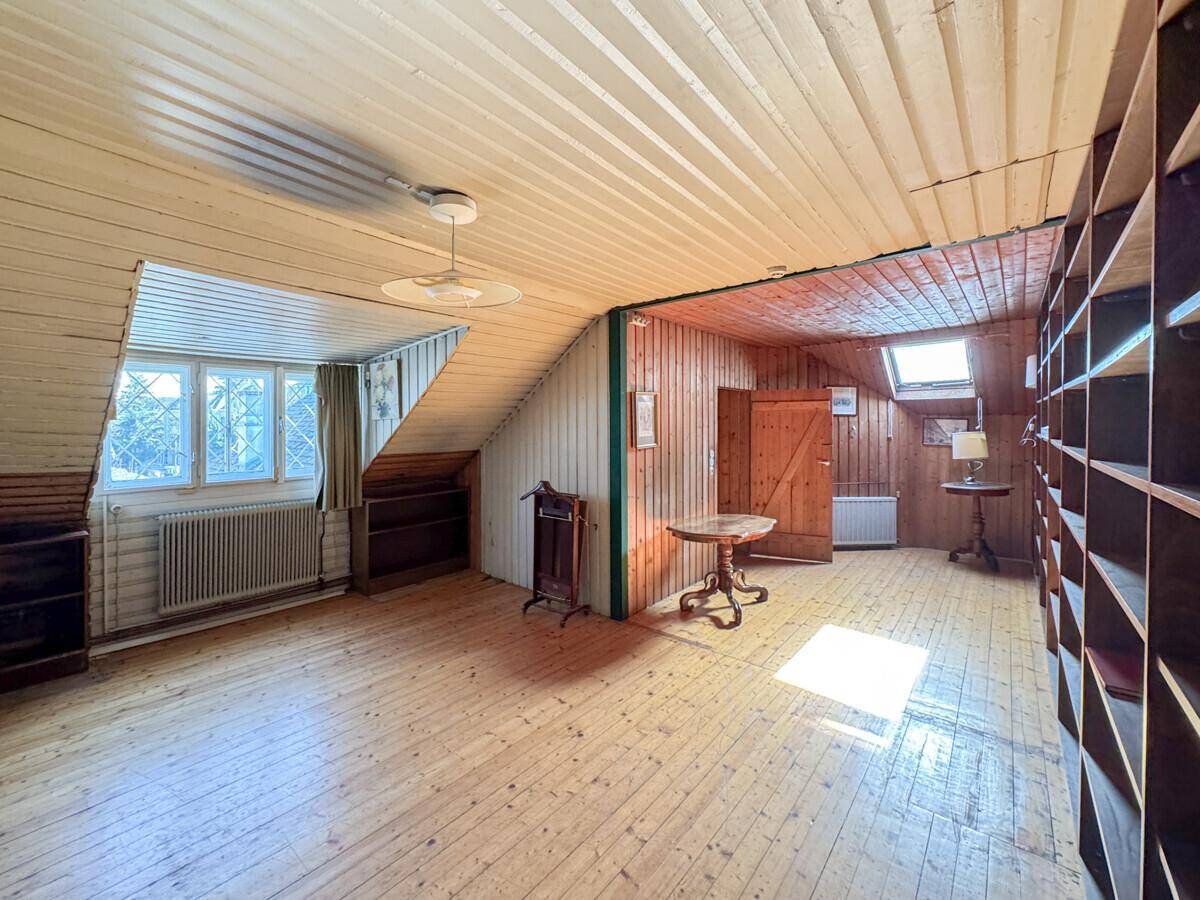 Gemütlicher Dachbodenraum mit Holzverkleidung, Dachschrägen, Holzdielenboden und einem Dachfenster.