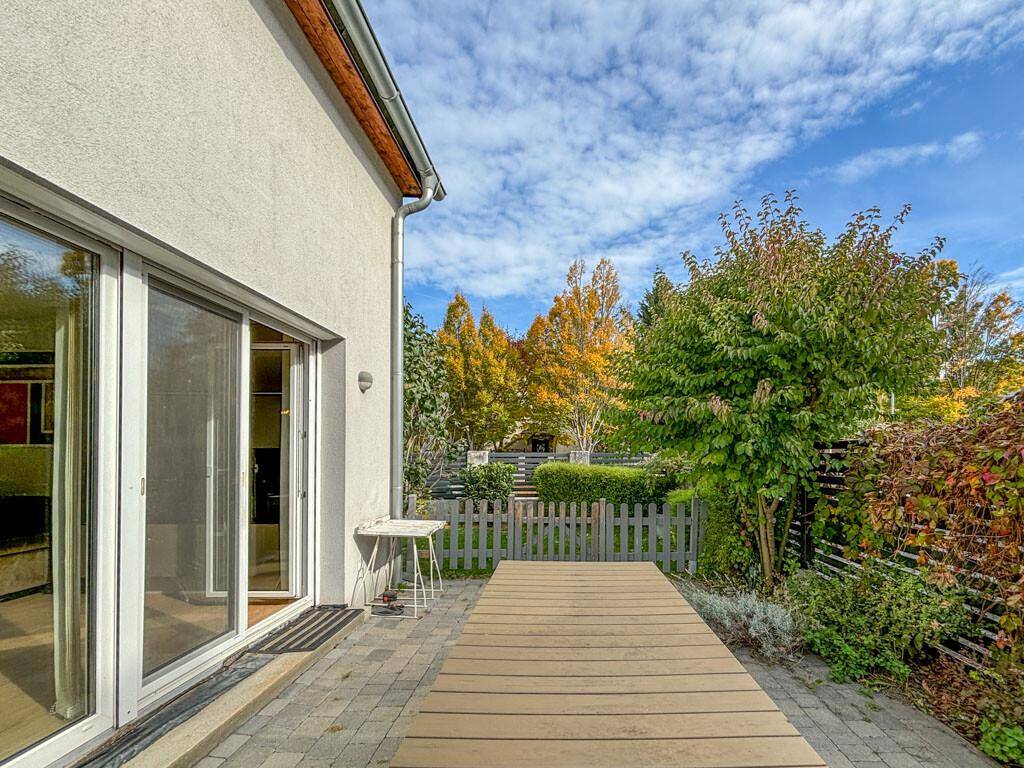 Gepflasterter Außenbereich mit einem Holztisch und Blick auf den grünen Garten.