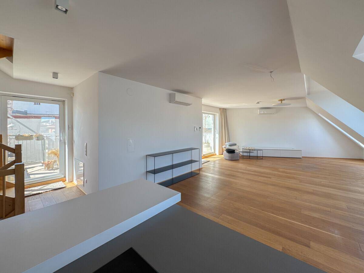 Geräumiger, offener Wohnbereich mit Holzboden, Kücheninsel und direktem Zugang zu einem Balkon.