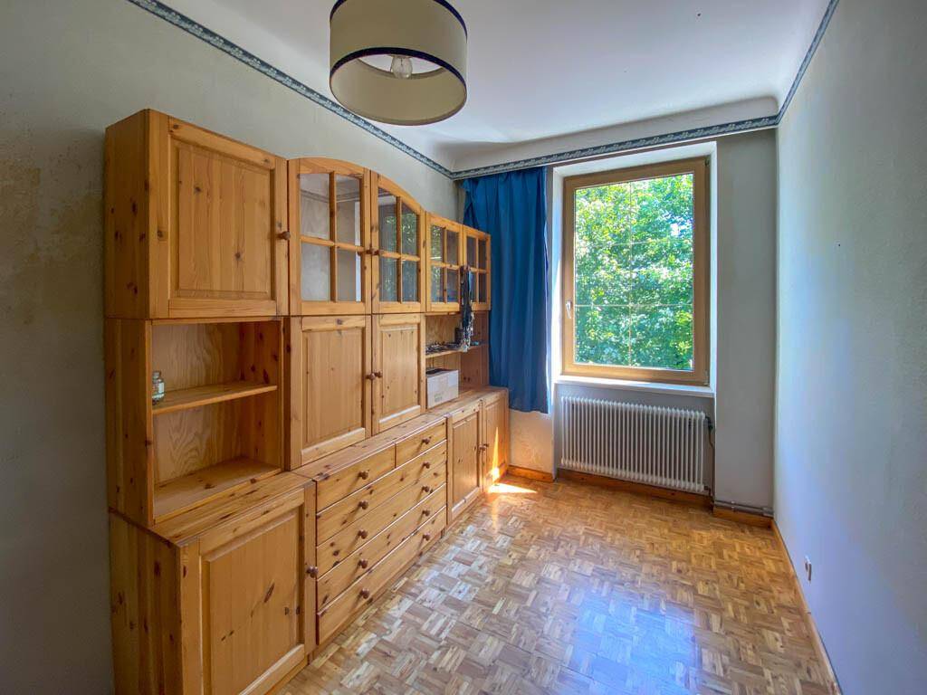 Schlafzimmer mit Holzboden, großem Holzschrank und Fenster mit Blick ins Grüne.