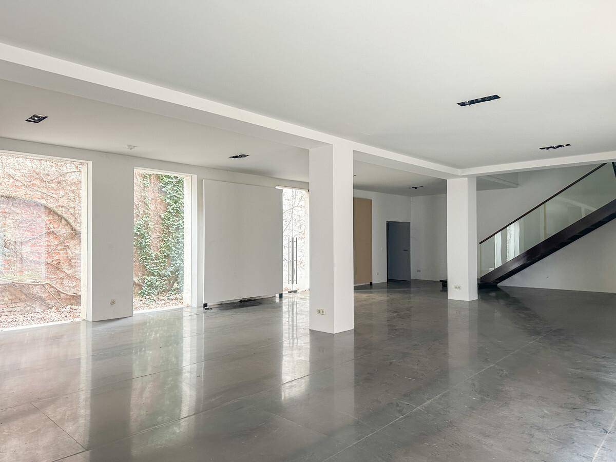 Geräumiger, leerer Raum mit Betonboden, weißen Wänden und einer modernen Treppe mit Glasgeländer.