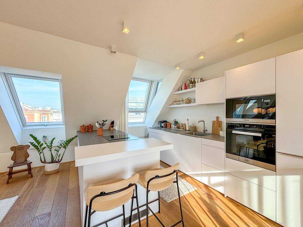 Moderne weiße Küche mit integrierten Geräten, Kochinsel und viel Tageslicht durch Dachfenster.